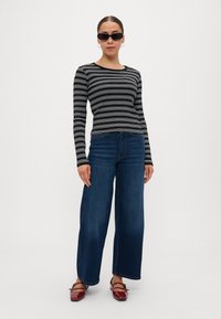 Black and white striped long-sleeve shirt, paired with wide-leg blue jeans. Model wears black sunglasses and red flat shoes.