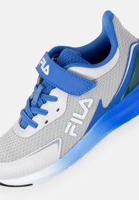 Scarpa atletica grigia con dettagli blu, parte superiore in rete, fascetta in Velcro e dettaglio del logo. Presenta una suola testurizzata per aderenza e supporto.