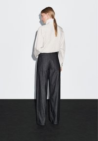 Svetle pruhovaná košile s vysokým límcem, doplněná volnými tmavými džíny. Jednoduchý design, neutrální barvy a pohodlný střih.