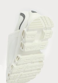 Bílé sportovní boty s vrškem z mesh a syntetického materiálu, zaoblený design, texturovaná gumová podrážka a výrazně tvarované sekce pro trakci.