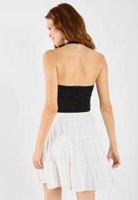 Top cropped negru tricotat cu un model texturat și gât halter, asociat cu o fustă albă, fluidă, cu pliuri. Material moale cu talie elastică.