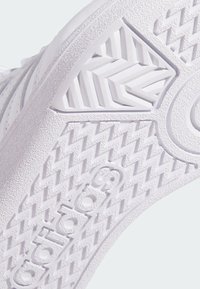 Bijela gumena podloga tenisica s teksturiranim uzorcima; sadrži zigzag dizajn i istaknutu oznaku. Glatka i izdržljiva površina.