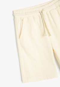Cremefarvede shorts med elastisk talje, snor og sidelommer. Tekstureret stof med et subtilt ribbet mønster.