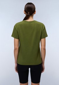 Olivgrünes Baumwoll-T-Shirt mit kurzen Ärmeln, Rundhalsausschnitt und geradem Schnitt. Kombiniert mit schwarzen, figurbetonten Shorts, die eine entspannte Passform zeigen.