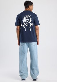 Camiseta de algodón azul marino con un gráfico blanco de una mano cruzando los dedos en la parte de atrás. Corte relajado, mangas cortas y cuello redondo.