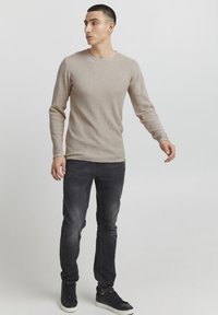 Beige ribbed long-sleeve shirt with a round neckline, paired with dark slim-fit jeans and black sneakers. Simple design, textured fabric.