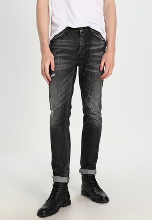 Czarne, dopasowane, postrzępione jeansy podwinięte przy kostkach, noszone z czarnymi botkami sznurowanymi i białym, wpuszczonym w spodnie t-shirtem.