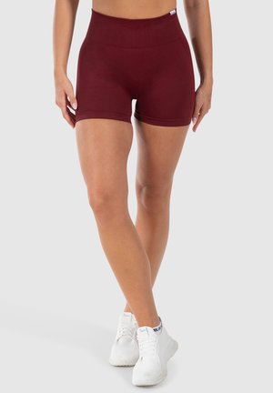 Pantaloni corti da atletica bordeaux con vita alta, texture liscia e design aderente. Abbinati a sneakers bianche per un contrasto.