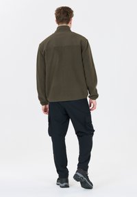 Olivgrön fleecejacka med en slät övre panel; parat med svarta cargobyxor med sidofickor och texturerade vandringsskor.