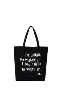Black tote bag with two handles, white handwritten text saying "I'm living my memoir. I don't need to write it." and small blue hashtag #KARLCORE.