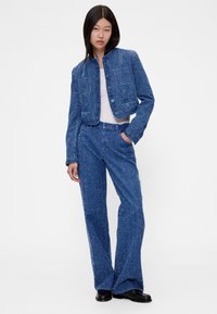 Sininen farkkutakki, jossa on tekstuuri ja etutaskut, yhdistetty vastaaviin leveälahkeisiin housuihin. Molemmissa vaatekappaleissa on erottuva kudonta.