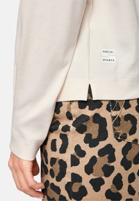 Beige geripptes Langarmoberteil mit seitlichem Schlitz, kombiniert mit braunen Leopardenmuster-Hosen, die schwarze Akzente und Nähdetails aufweisen.
