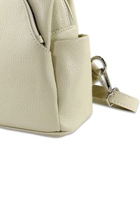 Sac en cuir beige clair avec une finition texturée, équipé d'une fermeture éclair et d'une sangle réglable avec un clip en métal argenté.