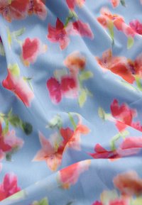 Hellblauer Stoff mit einem Blumenmuster aus rosa, orangefarbenen und grünen Blumen. Die Textur wirkt weich und leicht transparent.