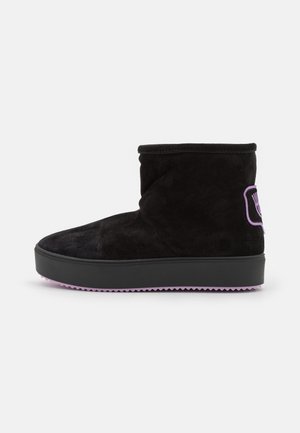 Stivale alla caviglia in suede nero con punta rotonda e suola viola. Presenta un piccolo dettaglio con logo viola sul lato esterno.