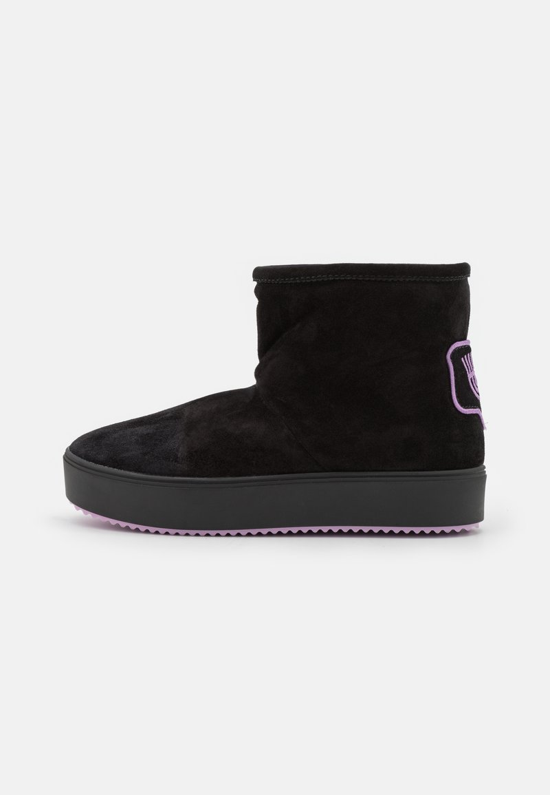 Bota de ante negra hasta el tobillo con punta redonda y suela morada. Presenta un pequeño detalle con el logo en morado en el lado exterior.