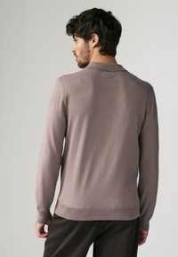 Licht mauve langmouw polo-shirt met een zachte textuur, voorzien van een geribde kraag en zoom, en een ontspannen pasvorm.