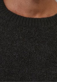 Pull tricoté de couleur foncée présentant une surface texturée et duveteuse ainsi qu'un col rond côtelé. La matière semble douce et dense.