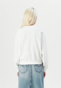 Felpa bianca dal taglio morbido, con polsini e orlo a coste, abbinata a una gonna di jeans azzurro chiaro con tasche posteriori.