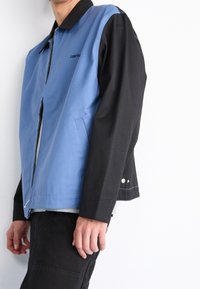 Blå og sort to-farvet jakke med lynlås foran, sidelommer og en kontrastfarvet krave. Fremstillet af et glat, robust stof.