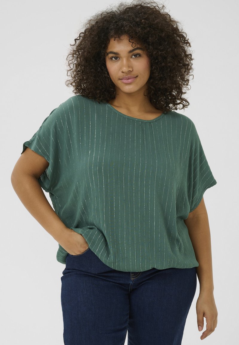 Blusa verde con rayas verticales, de mangas cortas y corte relajado. El material tiene un ligero brillo, combinada con jeans azul oscuro.
