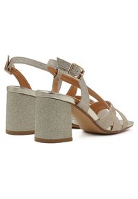 Sandali con tacco in oro lucido, caratterizzati da un tacco di glitter chunky, fasce incrociate e fibbia regolabile alla caviglia. Fodera interna morbida per il comfort.