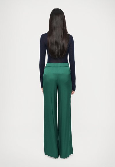 Tumesinist keha järgivat pika varrukaga topi, mis on kombineeritud laia jalaga smaragdroheliste pükstega, mis rõhutavad sujuvat, kerget tekstuuri ja elastset vöökohalt.
