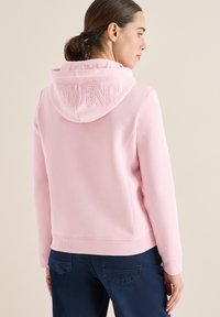 Felpa rosa con la scritta "MOMENT" ricamata sul retro. Tessuto morbido con una vestibilità comoda e polsini a coste, abbinata a pantaloni blu scuro.