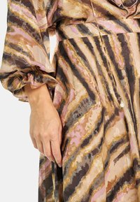 Vestido de estampado floral en tonos de rosa, marrón y dorado, con mangas largas abullonadas y tela fluida con un suave brillo.