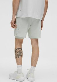 Ljust grå atletiska shorts med sidofickor, kombinerat med vita sneakers och ankelsockor. Synlig tatuering på benet.