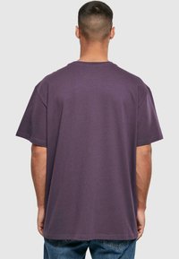 Lilla kortærmet t-shirt med en afslappet pasform, rund halsudskæring og en glat tekstur, parret med blå jeans. Bagfra vist.