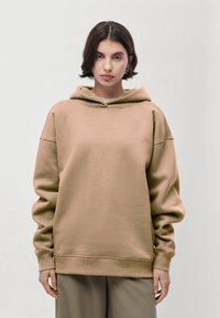 Felpa leggera beige realizzata in tessuto morbido, con una vestibilità comoda, maniche sovradimensionate e un piccolo logo ricamato sul davanti.