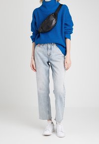 Niebieski dziany sweter z golfem, luźny krój; jasnoniebieskie dżinsy proste; czarna torebka na ramię; białe trampki.