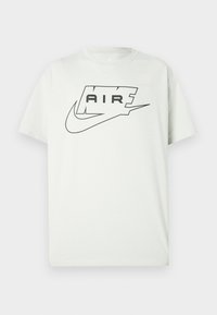 Tricou alb cu mânecă scurtă, cu logo-ul Nike Air negru, având cuvântul „AIR” în interiorul unui contur stilizat deasupra emblematicului swoosh.