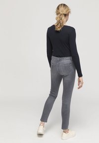 Grå denim slim fit jeans med medelhög midja, fem fickor och subtila blekningsdetaljer. Matchas med en svart långärmad topp och lätta skor.