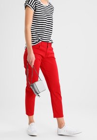 Červené kalhoty s úzkým střihem, spojené s černobílým pruhovaným tričkem. Bílá tenisky a malá šedá kabelka přes rameno dokončují vzhled.