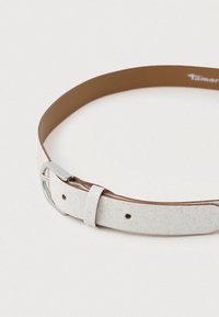 Biely trblietavý opasok s hladkým povrchom, ktorý má striebornú kovovú sponku a hnedú koženú podšívku. Sú viditeľné diery na nastavenie.