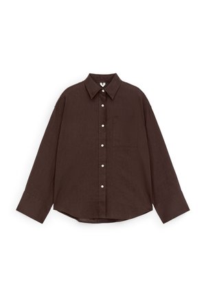 Chemise à manches longues marron foncé avec col pointu, poche poitrine avant et boutons blancs, posée à plat sur un fond blanc.