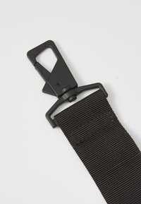 Cintura in nylon nero con un moschettone in plastica su un'estremità, distesa su uno sfondo bianco. La fibbia è progettata per un rapido rilascio.