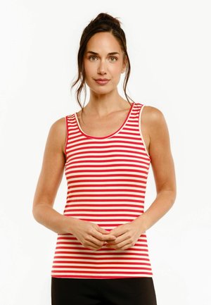 Femme portant un débardeur sans manches à rayures horizontales rouges et blanches, debout les mains vaguement croisées à la taille.