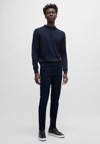 Jūrų laivyno ilgos rankovės polo marškiniai, siauras kirpimas, medvilnės ir sintetinio pluošto mišinys, apvalus kaklas. Dėvimi su tamsiai mėlynomis džinsinėmis kelnėmis ir juodais sportiniais batais su baltais pado akcentais.