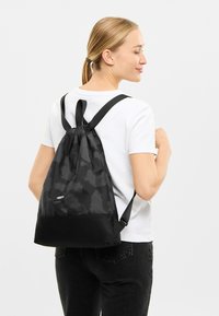 Rucsac negru cu șnur, cu un model texturat, fabricat dintr-un material ușor. Dispune de un fund solid negru și curele ajustabile.