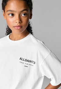 Bílá bavlněná tričko s černě potisknutým logem "ALLSAINTS" a japonským textem na levé části hrudi. Krátké rukávy, volný střih.