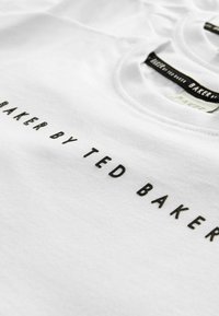 T-shirt en coton blanc comportant le texte "BAKER PAR TED BAKER" en broderie noire. Col rond avec une texture douce.