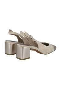Zapatos slingback de ante beige con un tacón bloque metálico plateado, punta afilada y tira en el tobillo ajustable. Textura suave y detalles mínimos.