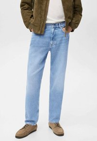 Jeans in denim azzurro chiaro con taglio dritto, caratterizzati da un classico design a cinque tasche e una leggera scoloritura, abbinati a scarpe in suede marroni.