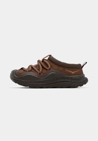 Zapatillas sintéticas marrones con parte superior acolchada, suela de goma texturizada y detalles de cordones en bucle. Incluye una presa en el talón y acentos en contraste.