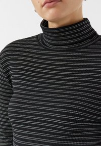 Czarny golf z poziomymi paskami w kolorze srebrnym i białym, wykonany z prążkowanej tkaniny. Posiada dopasowany krój i wysoką stójkę.