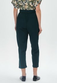 Zielone, wysokie spodnie z wąskimi nogawkami, z podwiniętym dołem i dwiema tylnymi kieszeniami. Noszone z wzorzystą bluzką z krótkim rękawem.