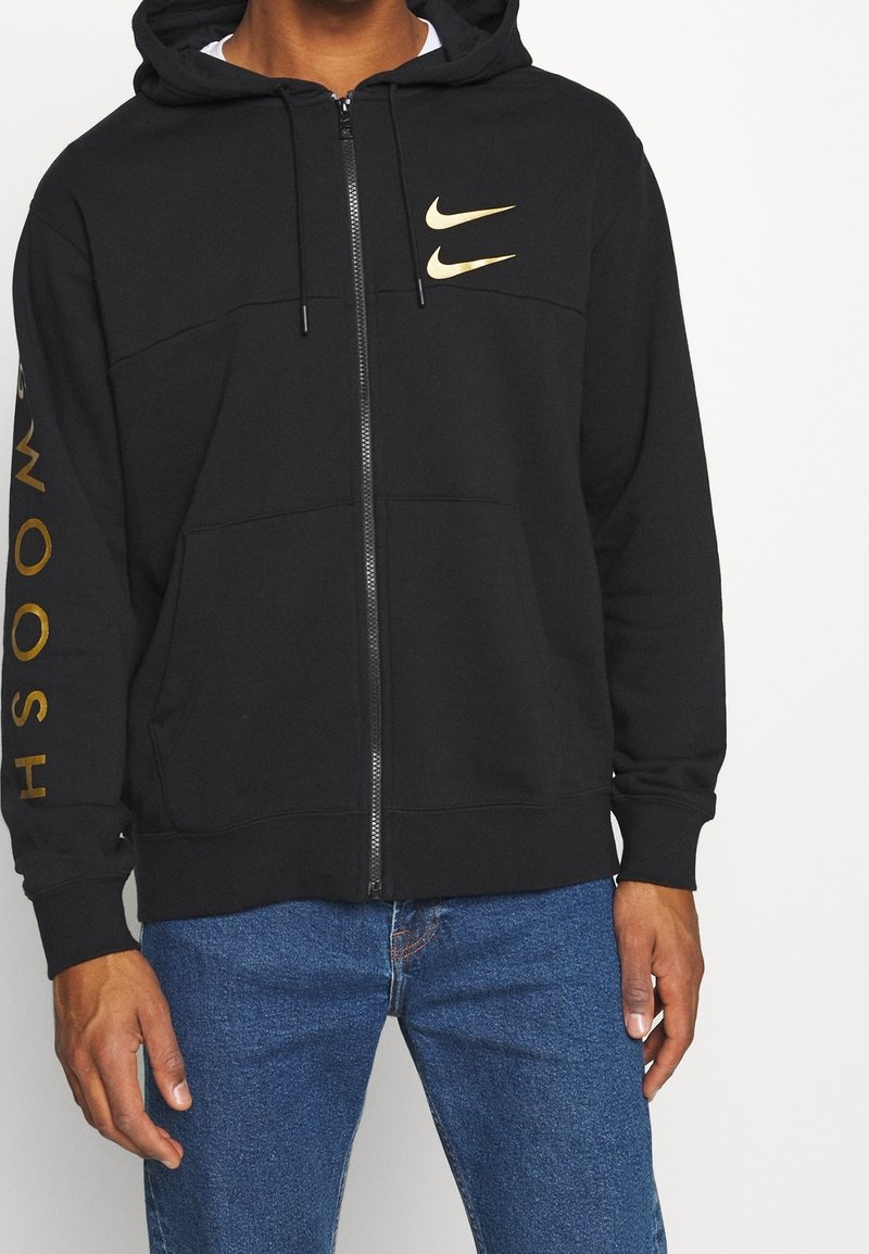 Black zip-up hoodie made of cotton blend, featuring a front pocket, drawstring hood, and gold Nike logo on chest and sleeve.
